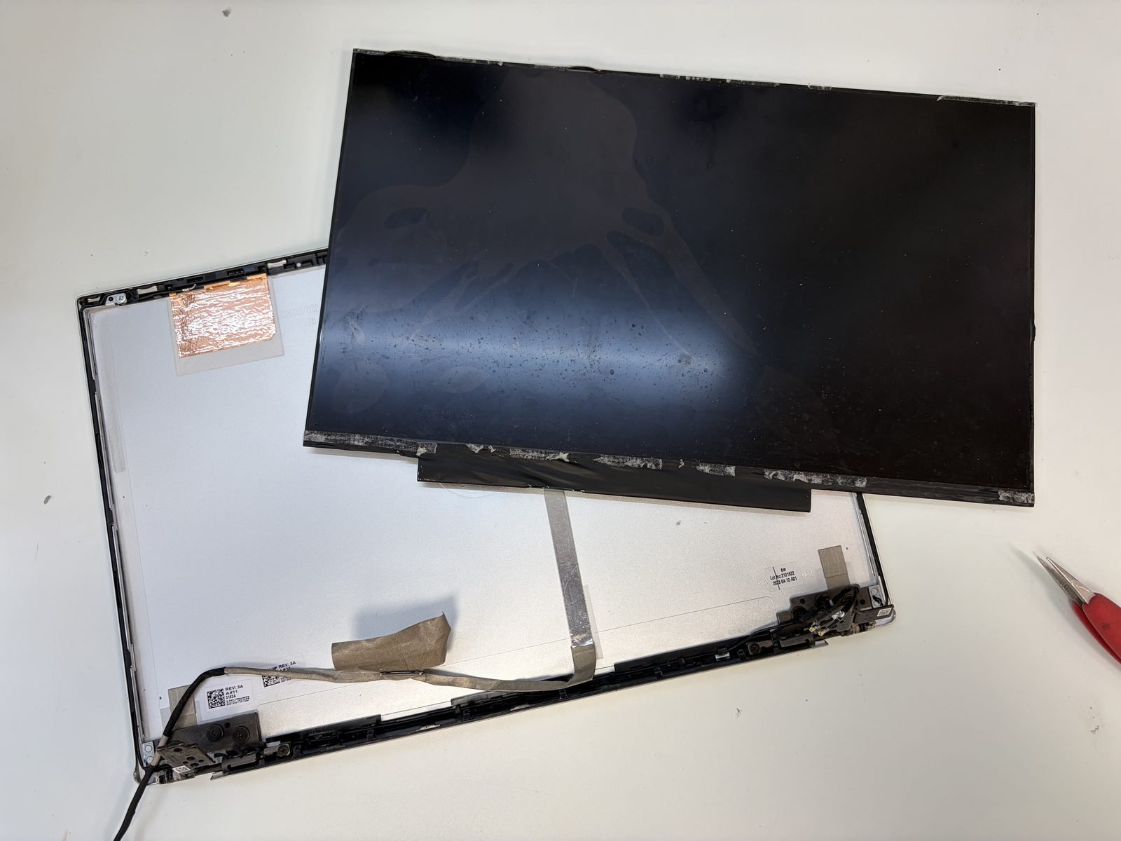 Het gedemonteerde LCD-paneel naast de schermbehuizing van de HP Pavilion, met de eDP-schermkabel en de scharnieren zichtbaar