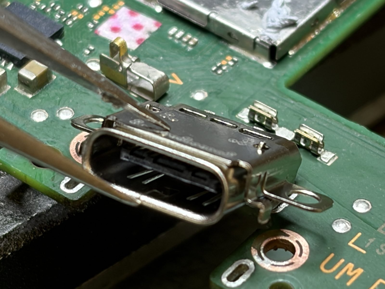 Een nieuwe USB-C-oplaadpoort wordt met een pincet op de soldeerpads van de Nintendo Switch OLED uitgelijnd
