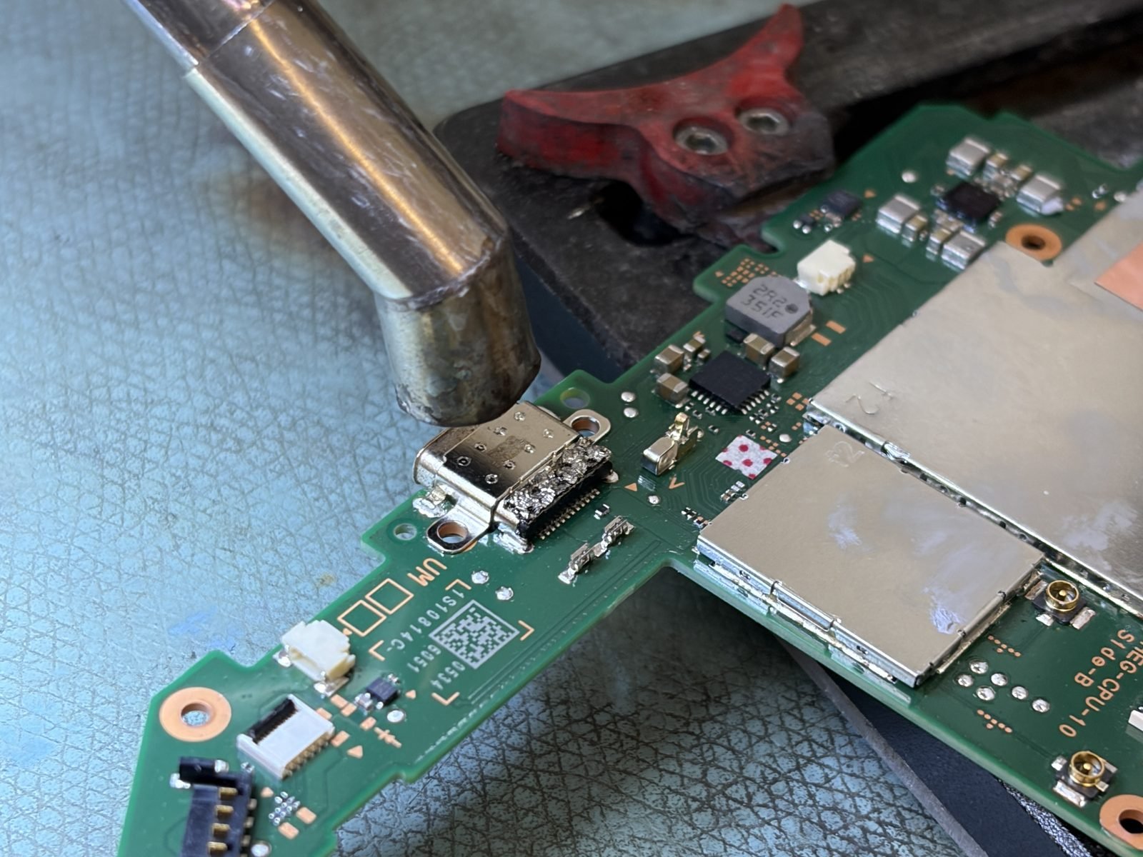 De nieuwe USB-C-oplaadpoort wordt op het moederbord van de Nintendo Switch OLED gesoldeerd met een soldeerbout